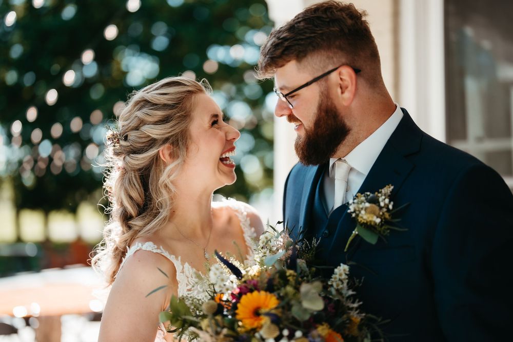 Joyful bride and groom laughing together, bride holding colorful bouquet with sunflowers on their wedding day.