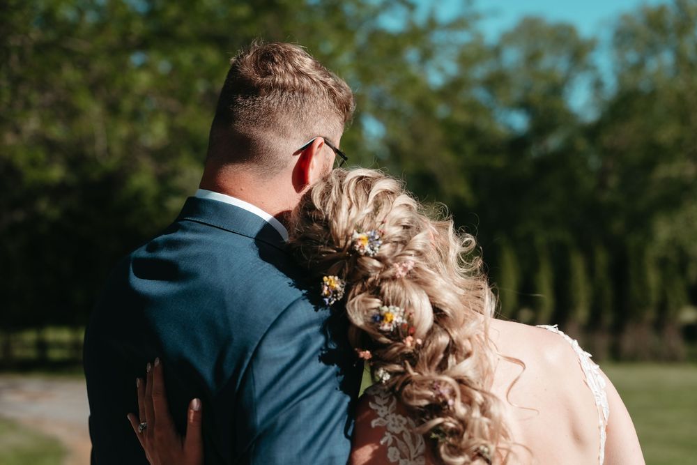 Bride and groom walking together from behind, bride with floral hair accessories in sunny garden setting.