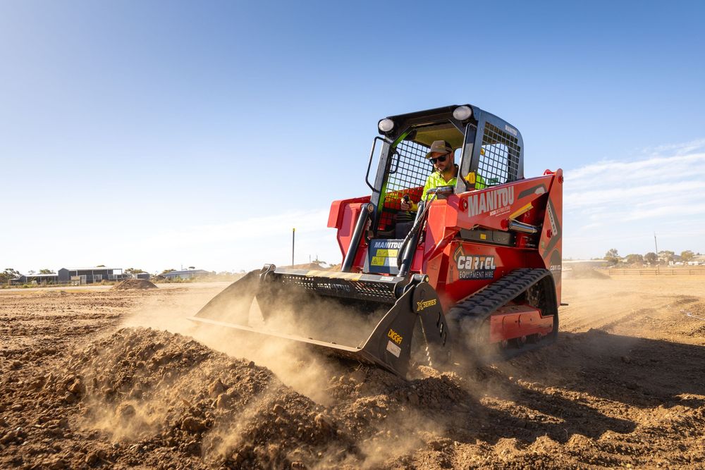 Red skid steer loader grading dirt on a construction site under a clear blue sky.