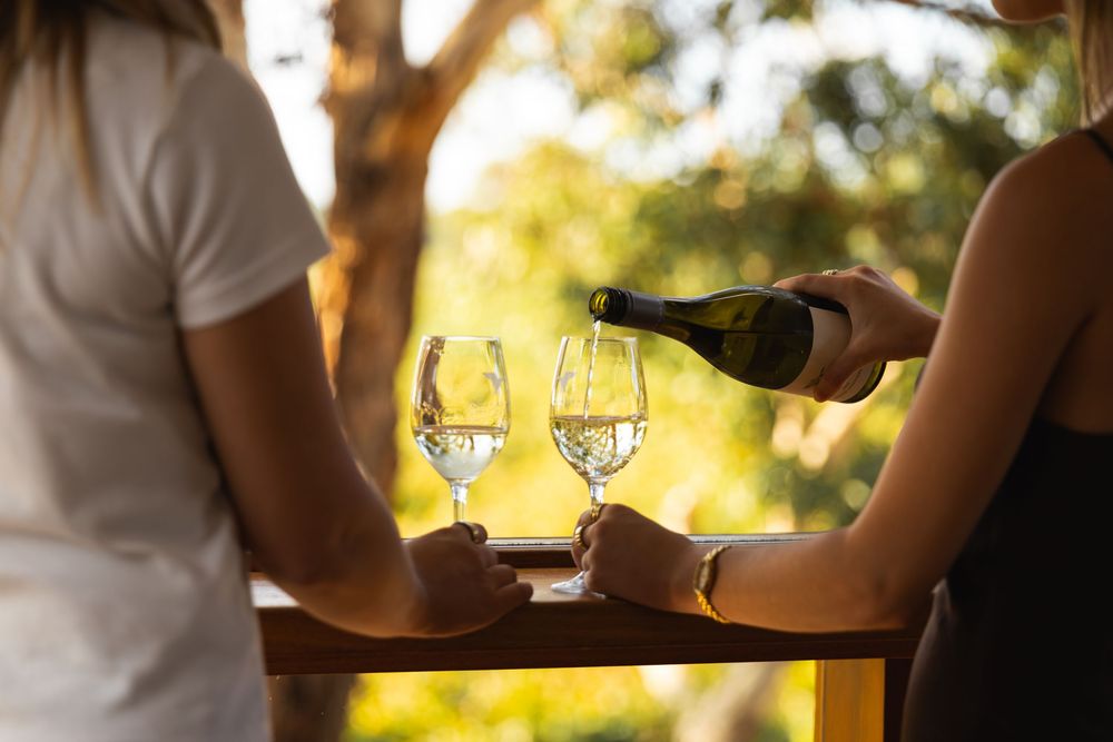 Woman pouring white wine into glasses on a balcony.