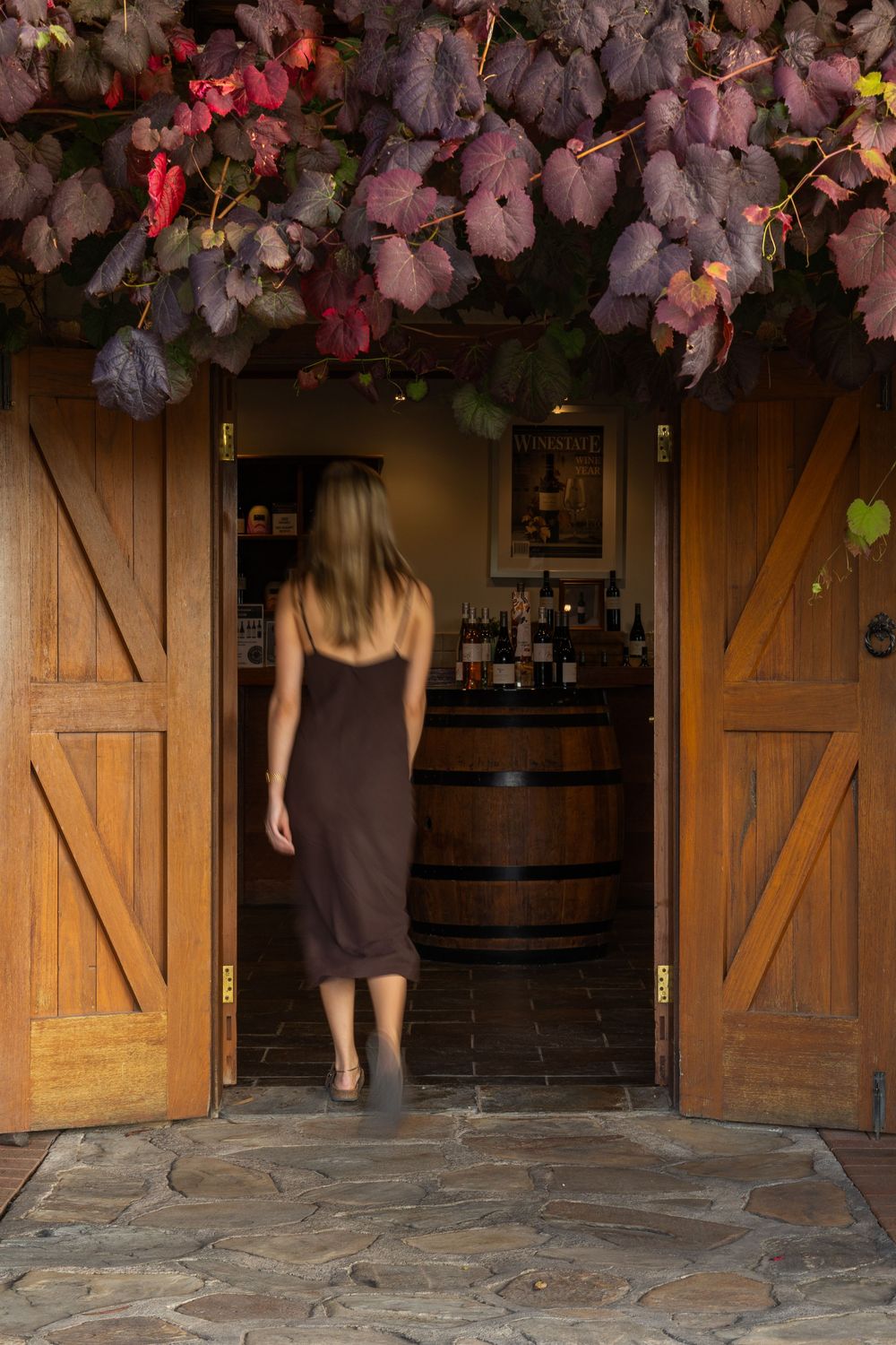 Woman in brown dress walking through rustic wooden barn doors into a winery cellar door.