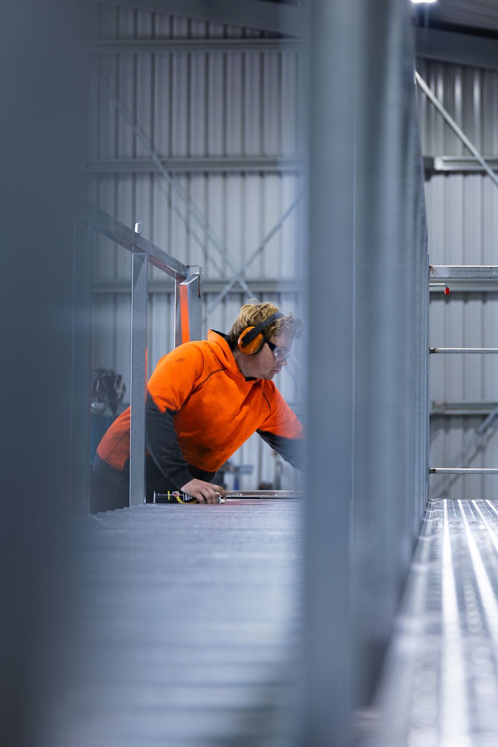 Worker in orange hi-vis uniform inspecting metal components inside an industrial facility.