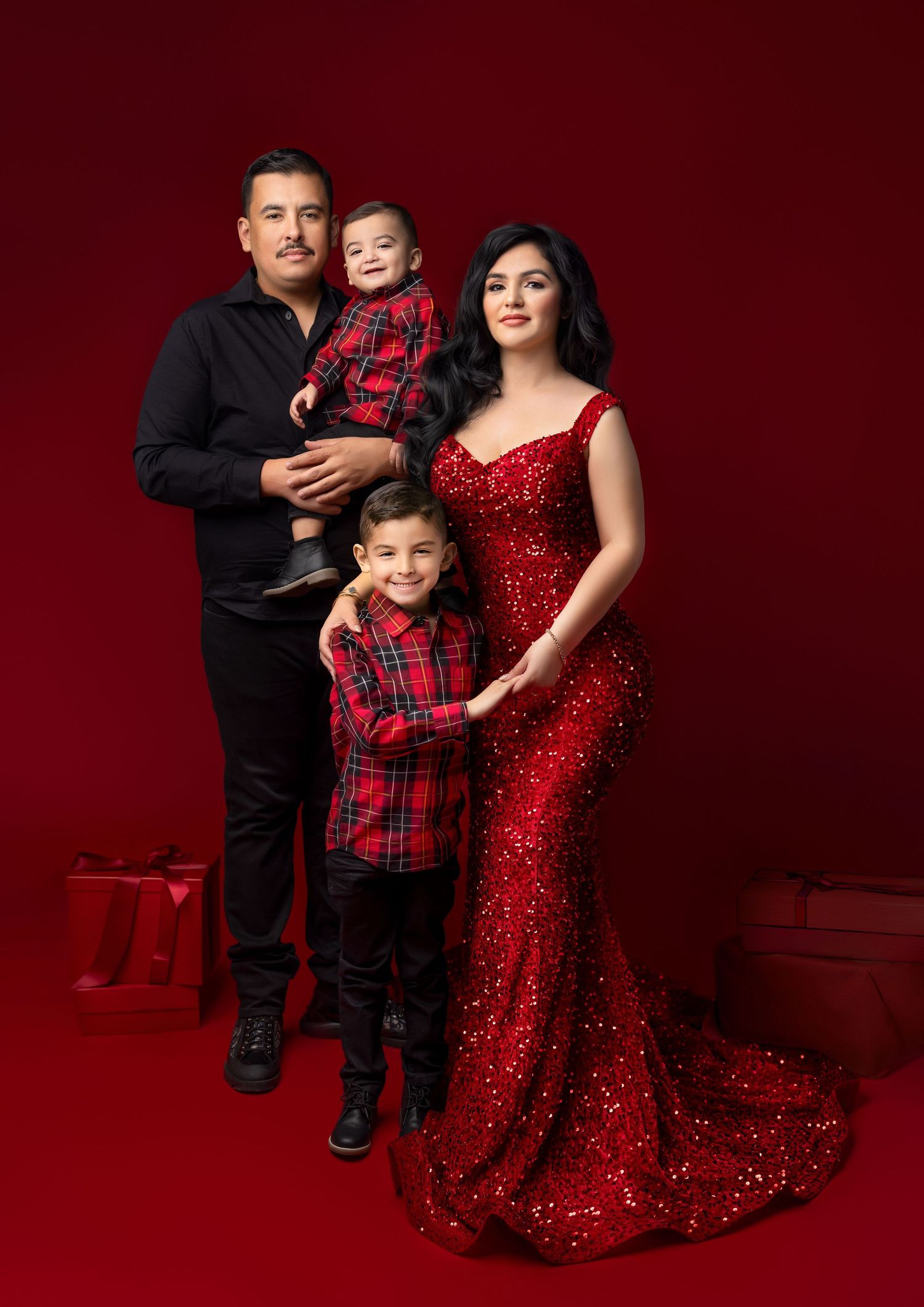 Family holiday portrait in red, pregnant mother in sequin gown, father holding toddler, young boy posing together.