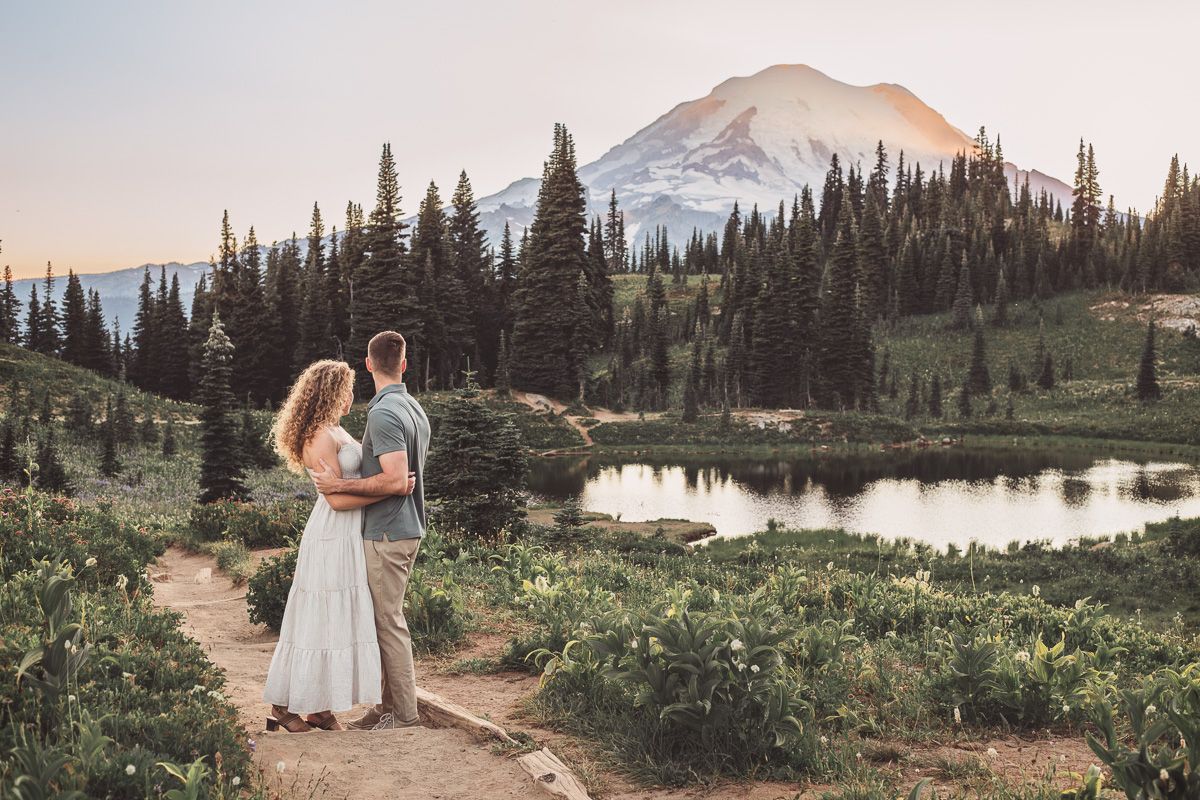 Couple standing together overlooking a scenic alpine lake with Mount Rainier and evergreen forest.
