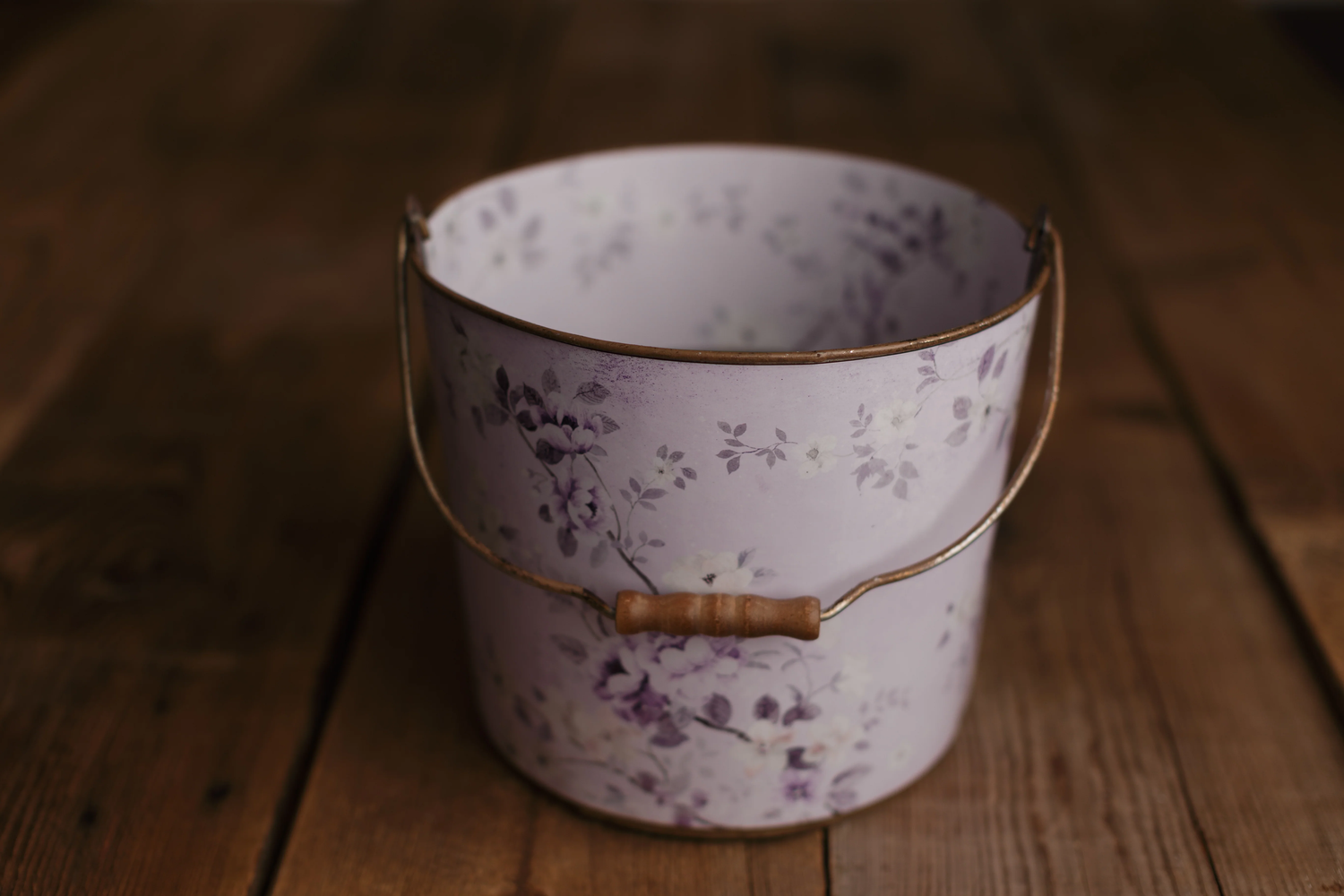 Lavender metal bucket with purple floral pattern and bamboo handle on wood.