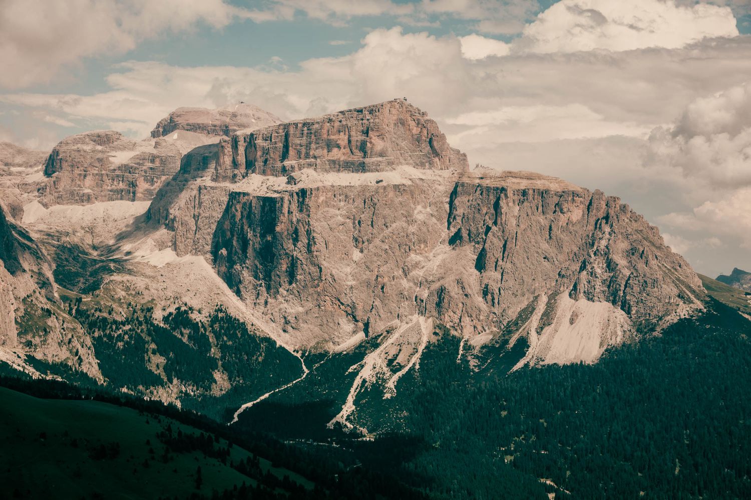 Dramatic rocky mountain peaks with snow-dusted slopes under a cloudy sky in the Dolomites, Italy.