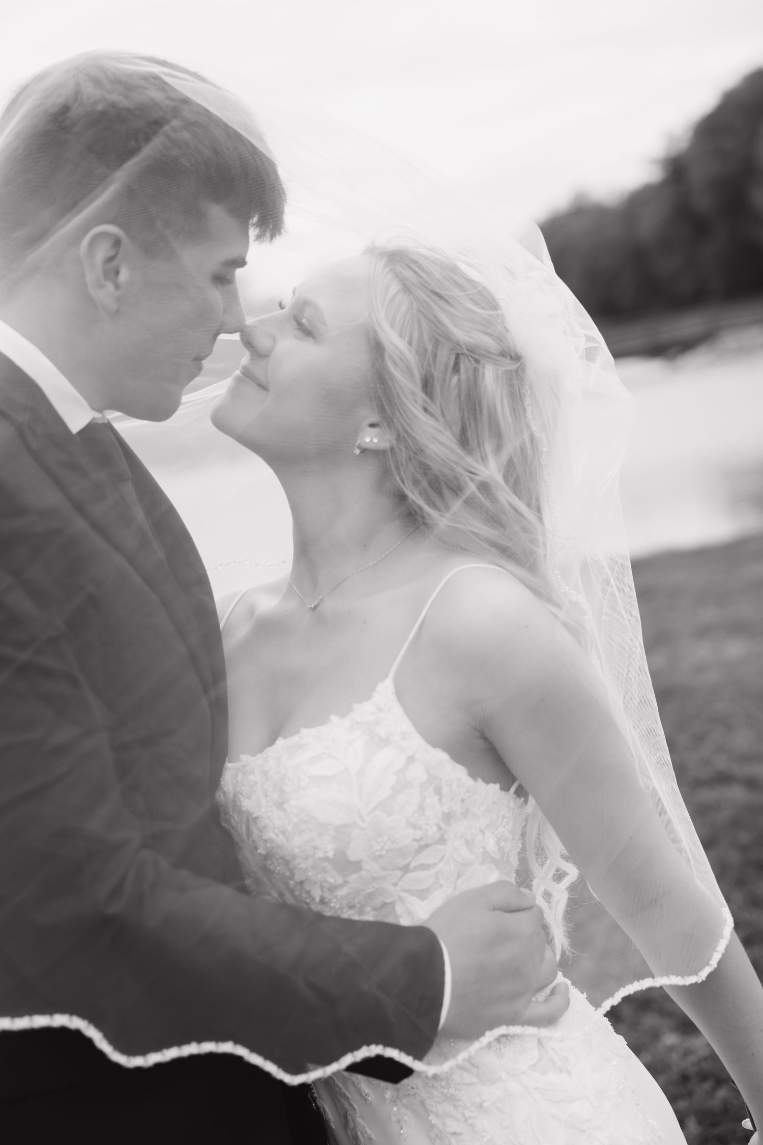 Bride in white gown smiles at groom during outdoor wedding ceremony with bridesmaids in black dresses.