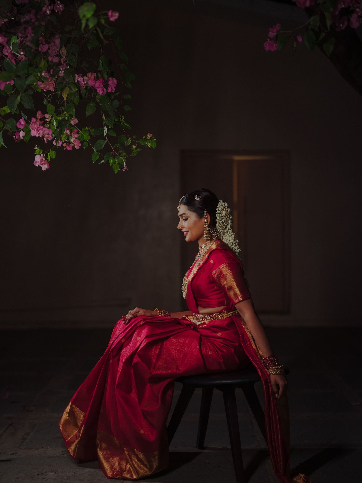 Indian bride in gold saree framed by large wooden doors at traditional wedding ceremony.