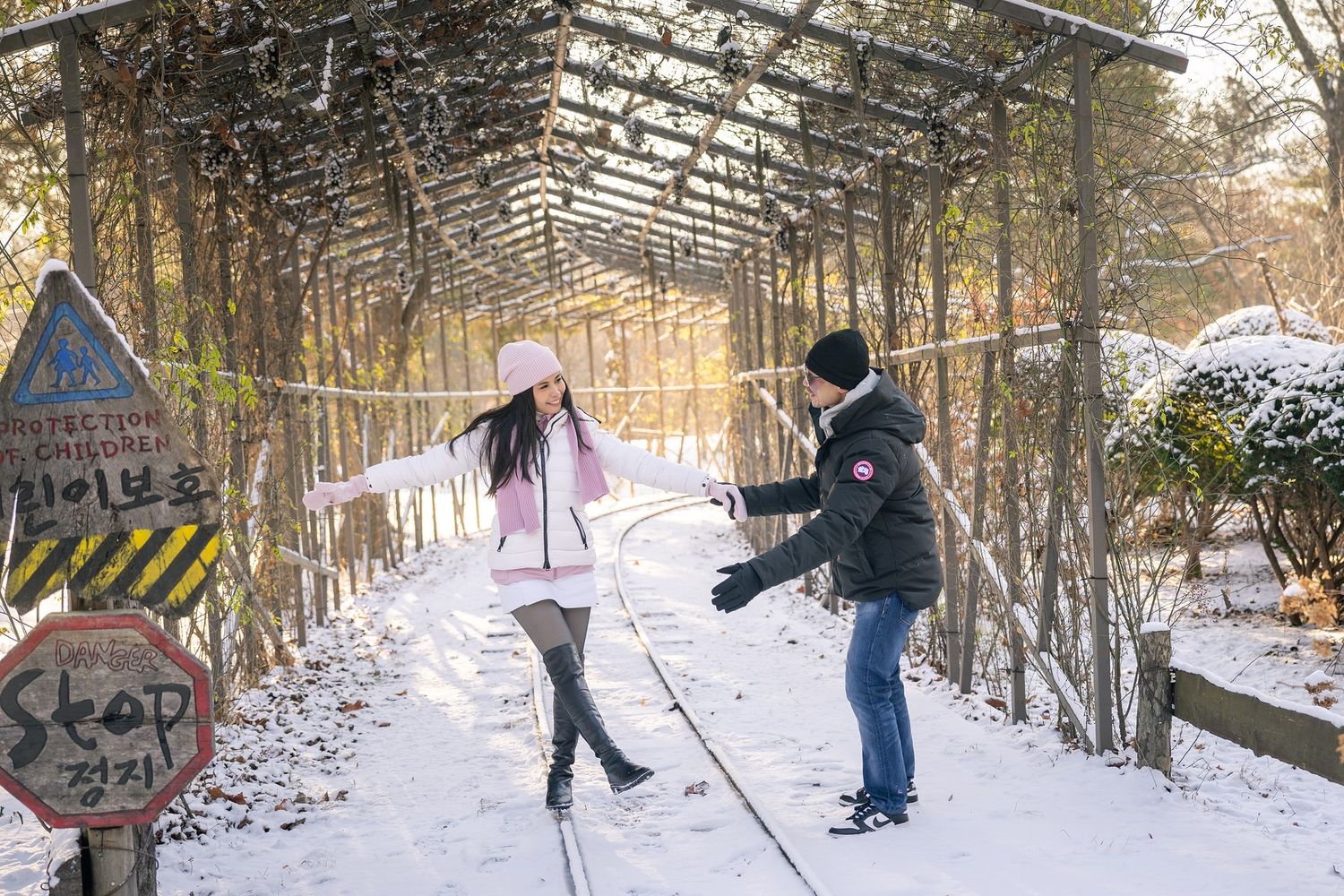 Couple playing in snow on a railway path under a pergola in a winter forest in Korea.