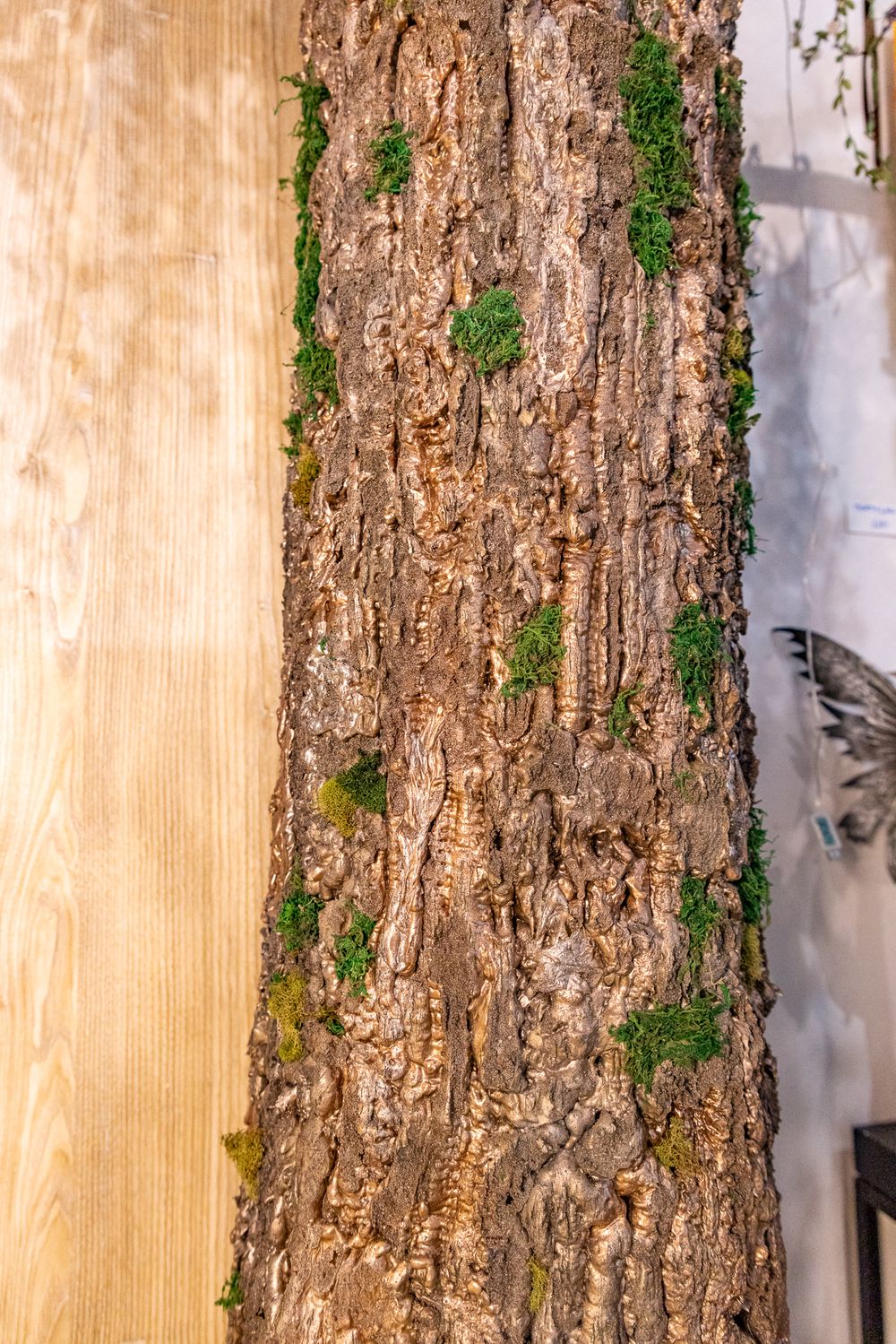 Close-up of rough tree bark with green moss patches, beside a smooth light wood panel surface.