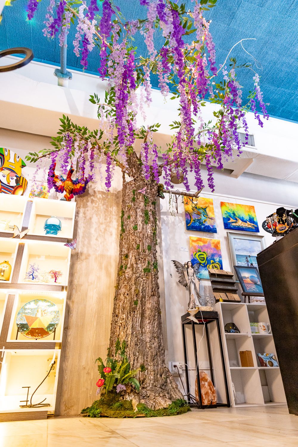 Decorative artificial wisteria tree with purple flowers in a colorful art gallery shop interior.