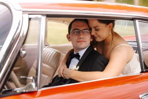 Bride and groom share a romantic moment inside a vintage orange classic car on their wedding day.