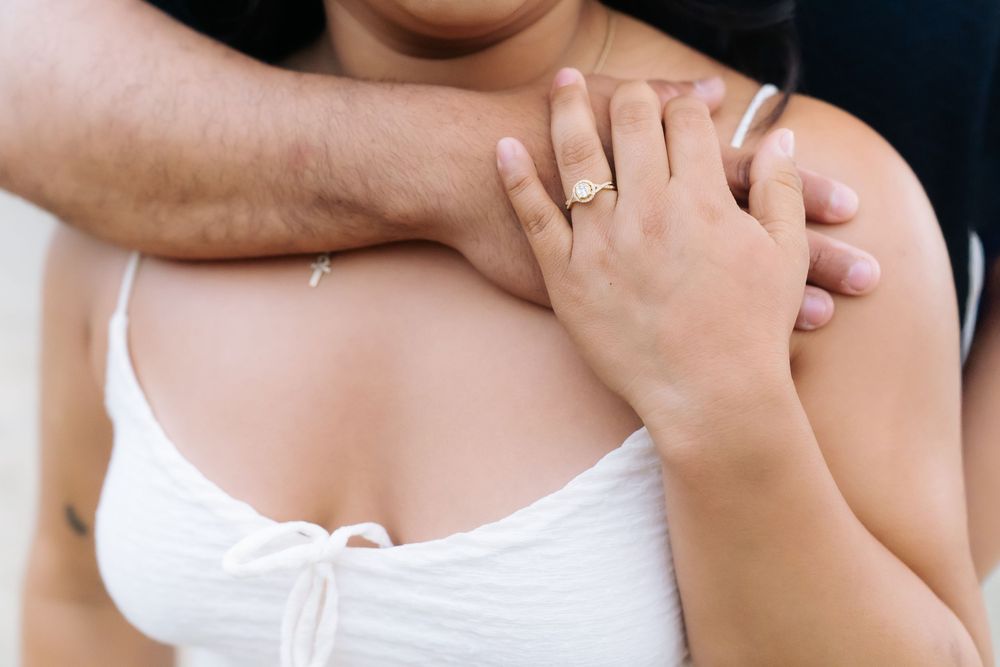Close-up of a couple embracing, woman wearing a gold engagement ring on her hand resting on her shoulder.