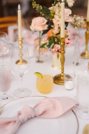 Elegant wedding table setting with gold candlesticks, pink flowers, a margarita cocktail, and blush pink linen napkin.
