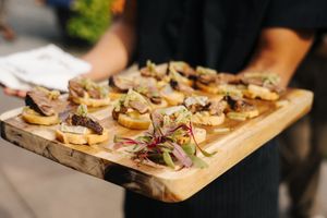 Elegant bruschetta appetizers on a rustic wooden serving board at a catered event.
