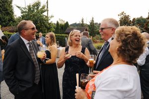 Guests in formal attire laugh and socialize outdoors at an elegant evening wedding reception.