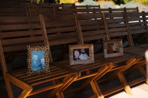 Three framed family photos displayed on wooden folding chairs at an outdoor wedding ceremony venue.