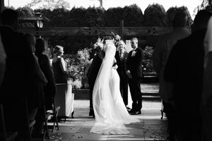 Black and white wedding ceremony photo showing bride and groom at the altar surrounded by guests outdoors.