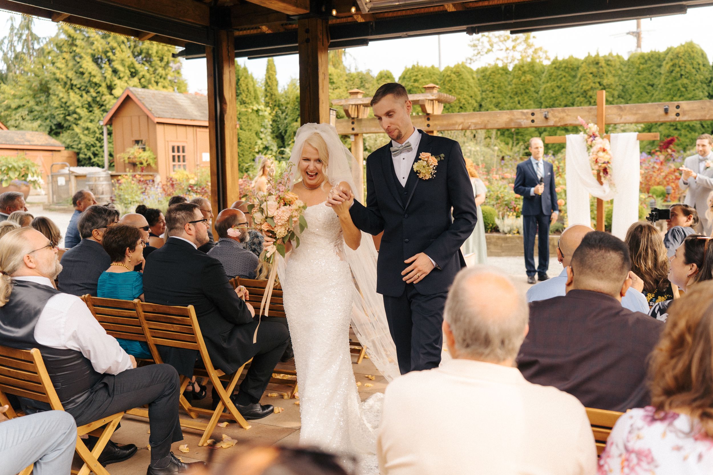 Bride and groom walk down the aisle together during an outdoor wedding ceremony with seated guests.
