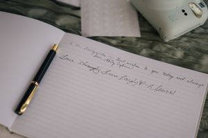 Open journal with handwritten love letter and black gold-tipped pen resting on lined pages, placed on a bed.
