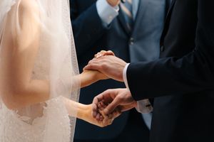 Bride and groom exchanging rings during wedding ceremony, close-up of hands holding rings in elegant formal attire.