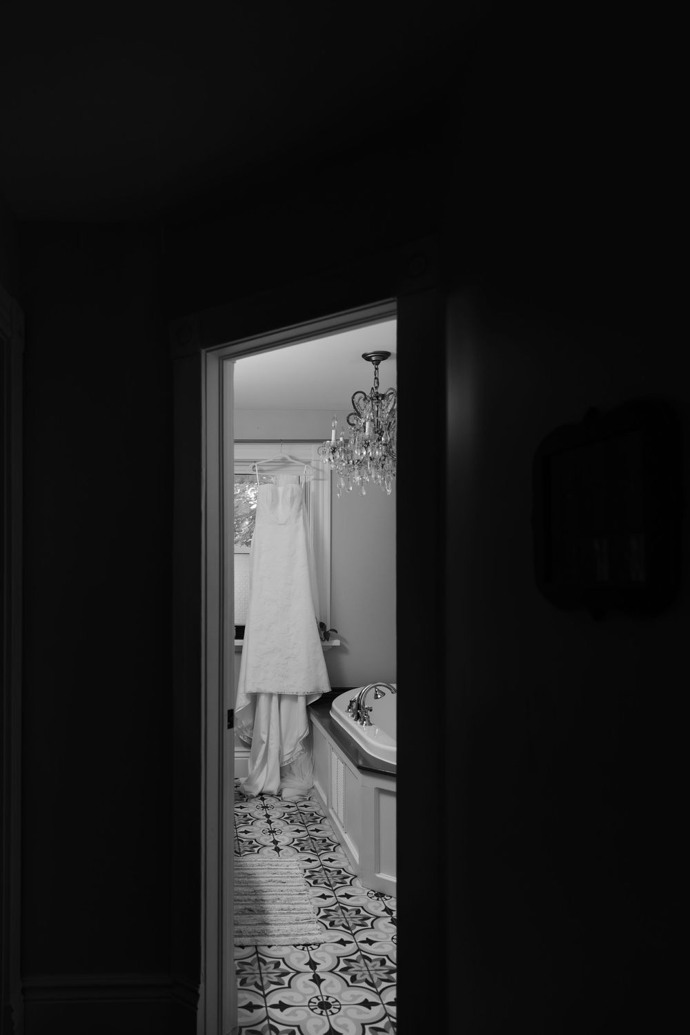 Black and white photo of bridal details including a brides dress hanging in the window of the during the wedding morning in london, ontario