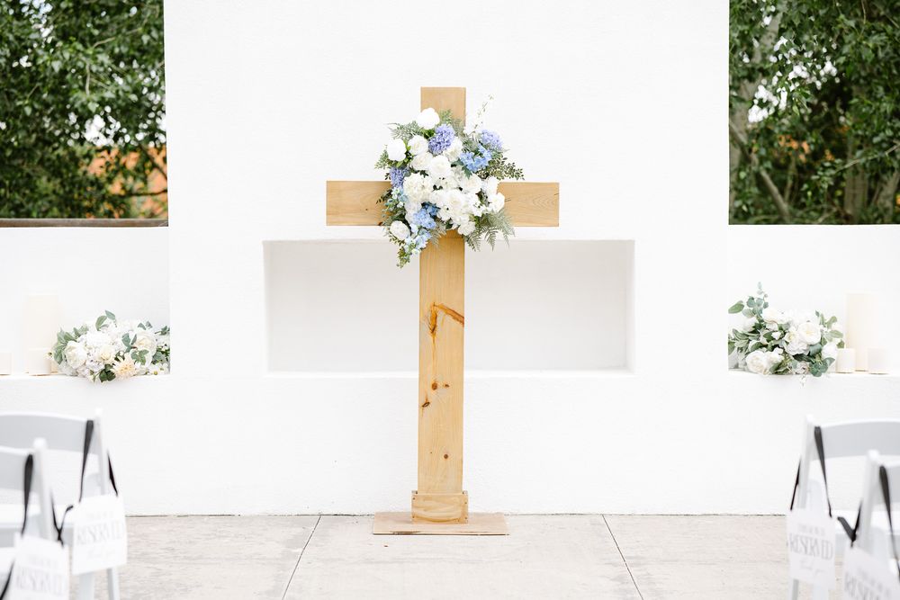 Wooden cross decorated with blue and white floral arrangement at outdoor wedding ceremony altar.