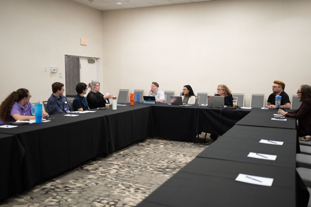 Group of professionals seated around U-shaped conference table in modern meeting room for business discussion.