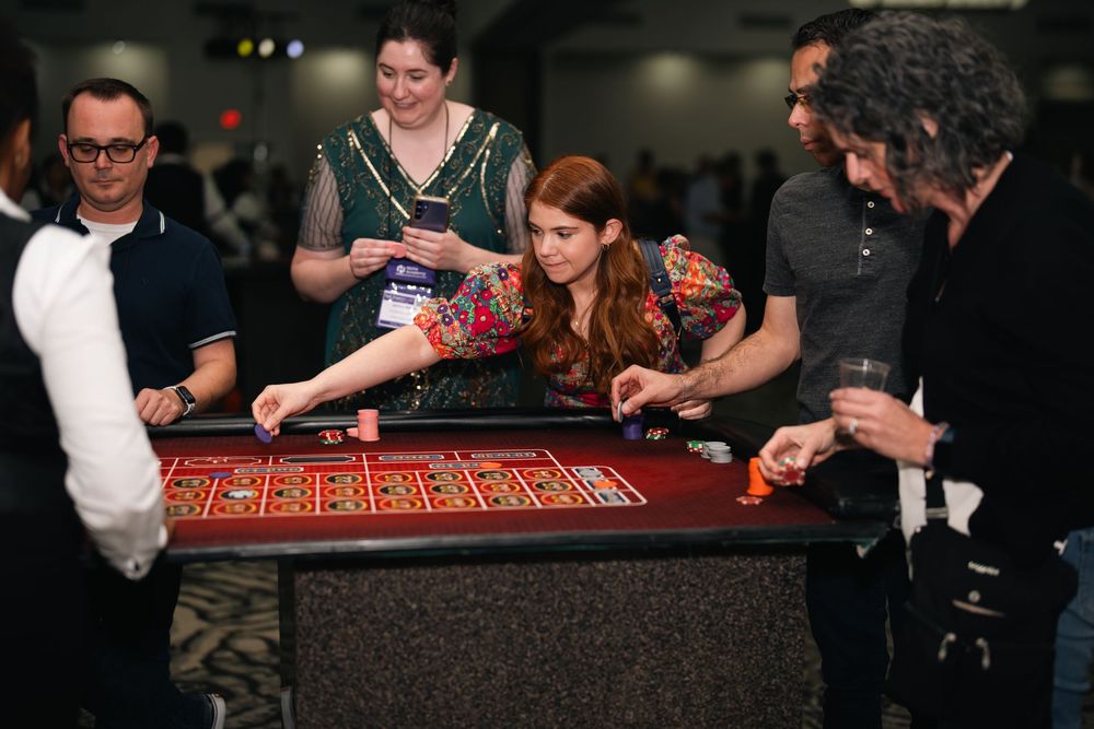Group of adults playing roulette at a casino night event, with a woman in colorful dress placing bets.