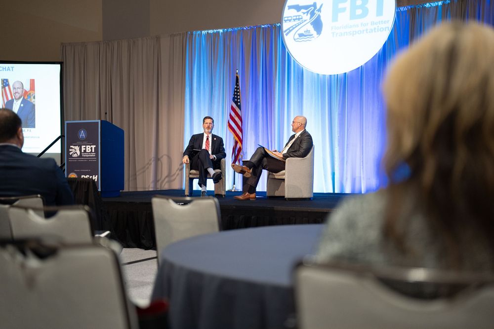 Two executives in discussion on stage at FBT conference with American flag and branded backdrop.