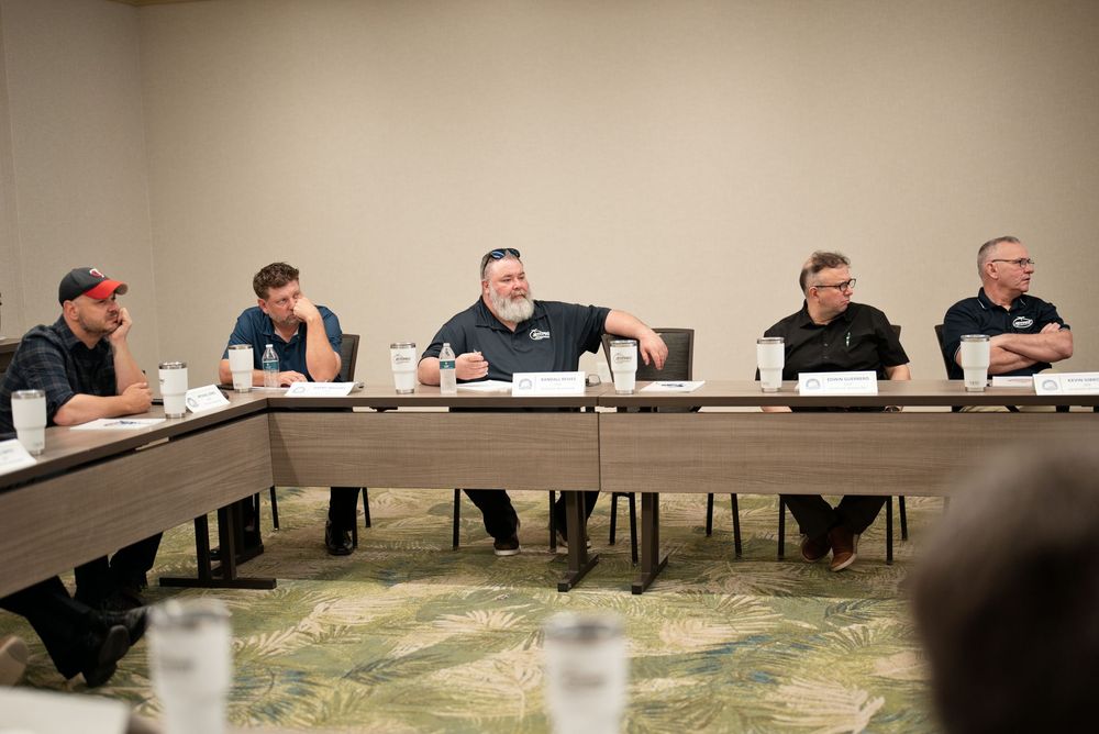 Five men seated at a conference table during a professional panel discussion in a meeting room.