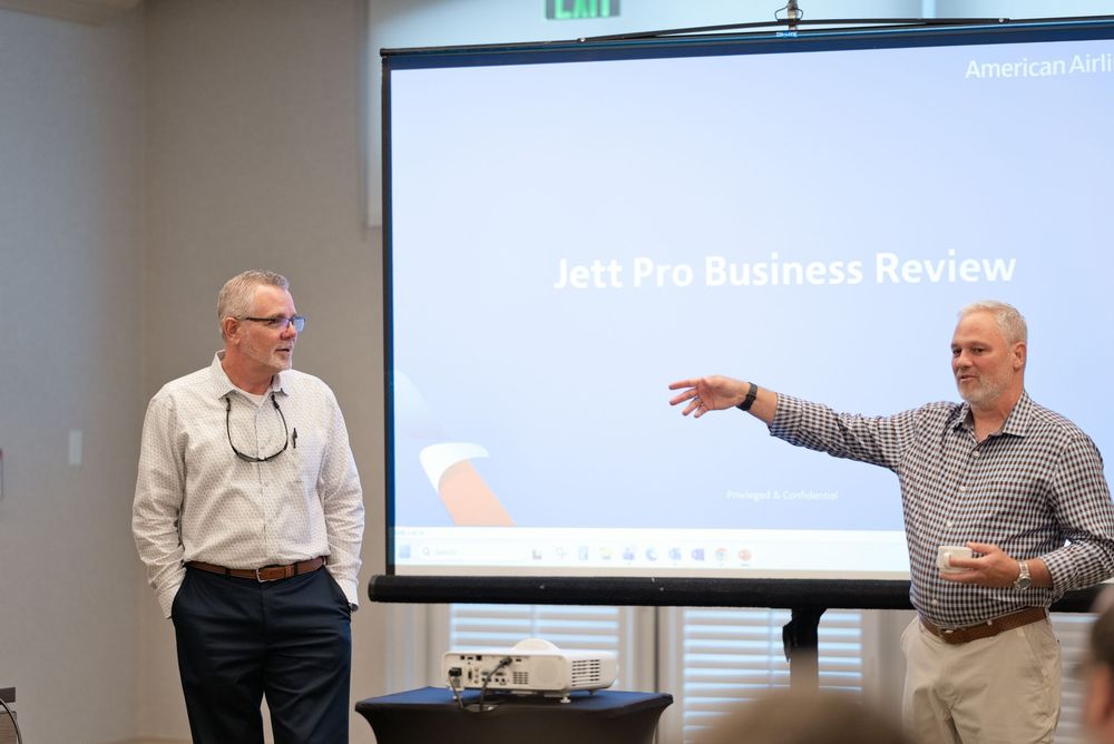 Two businessmen presenting Jett Pro Business Review on a projector screen in a corporate meeting room.