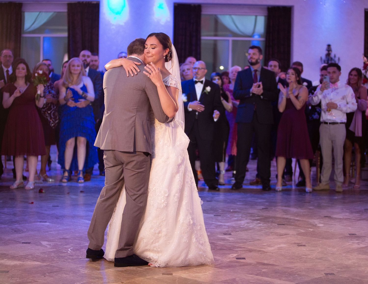 Bride and groom share their first dance at elegant wedding reception with guests applauding in background.