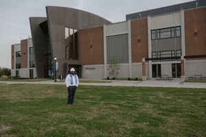 Person in hard hat stands on green lawn before modern brick and concrete university building.