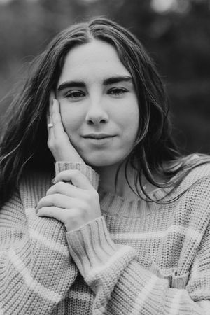 Black and white portrait of a young woman in a knit sweater, resting her cheek on her hand, gazing softly at the camera.
