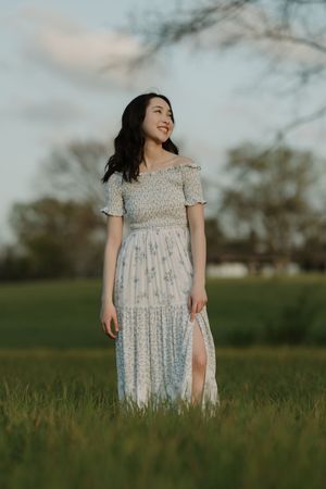 Young woman in floral off-shoulder maxi dress smiling in green field at golden hour.