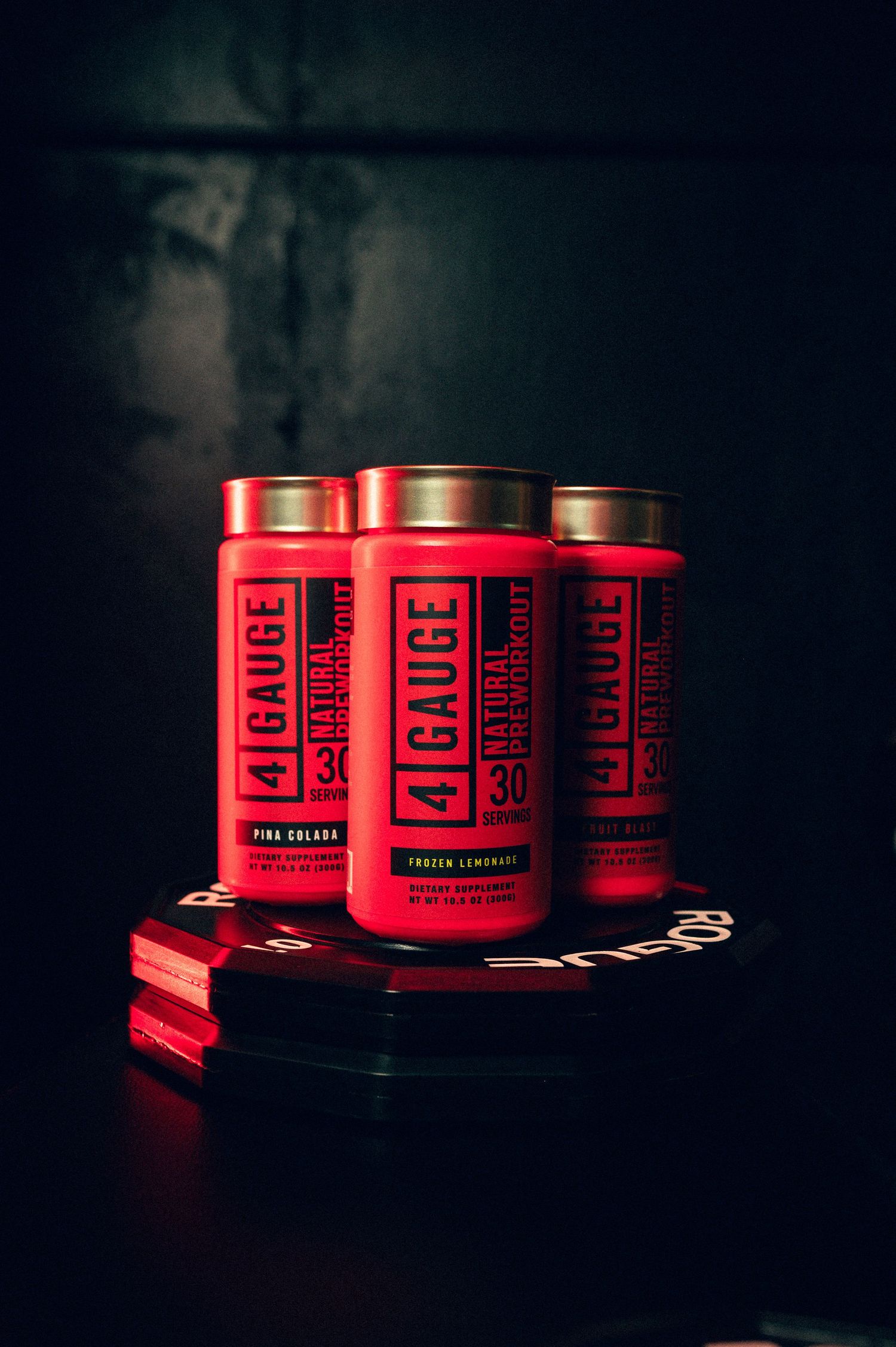Three red 4 Gauge natural pre-workout supplement containers in Pina Colada and Frozen Lemonade flavors on dark background.