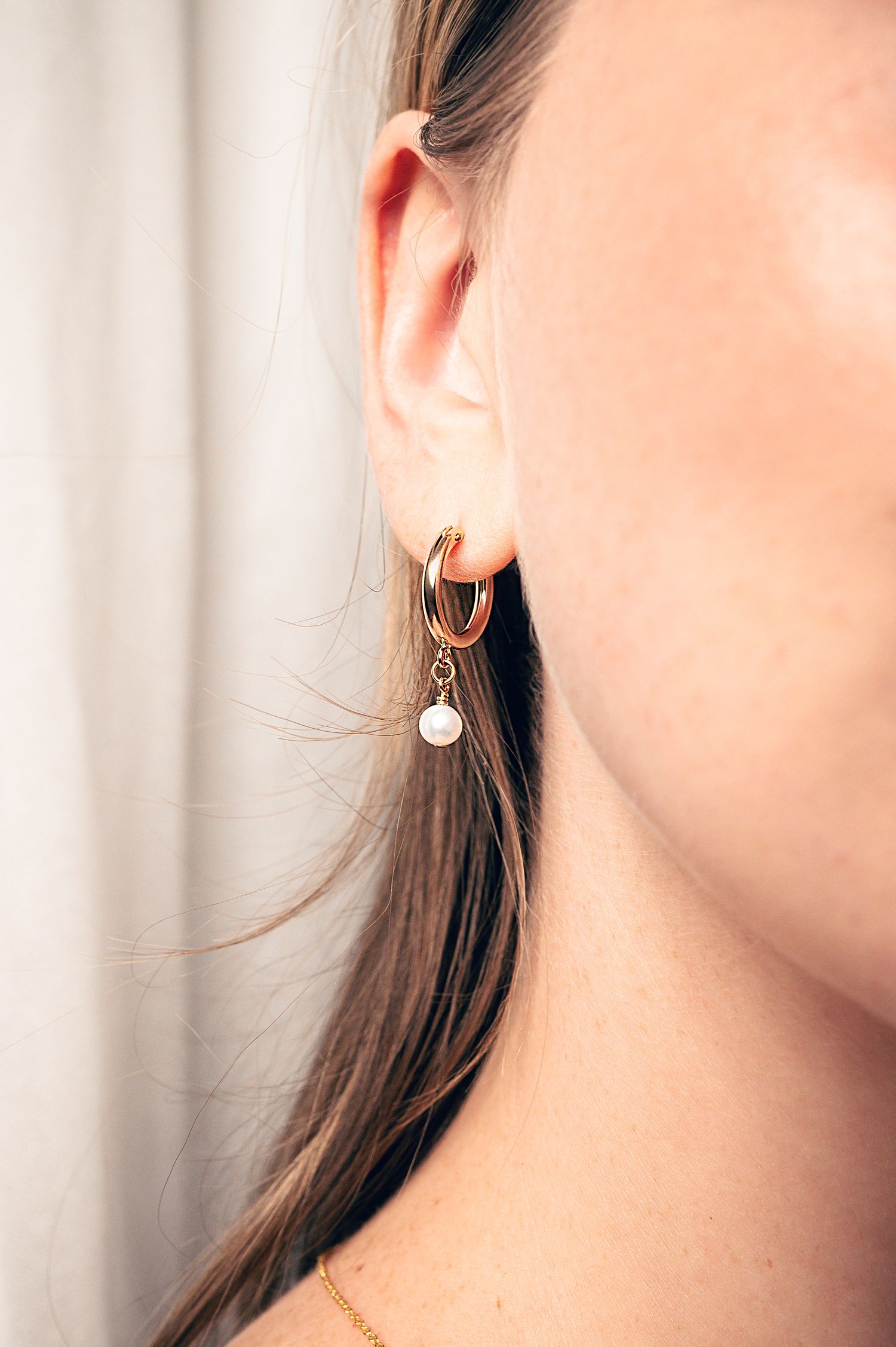 Gold hoop earring with pearl drop charm worn by a woman with brown hair.