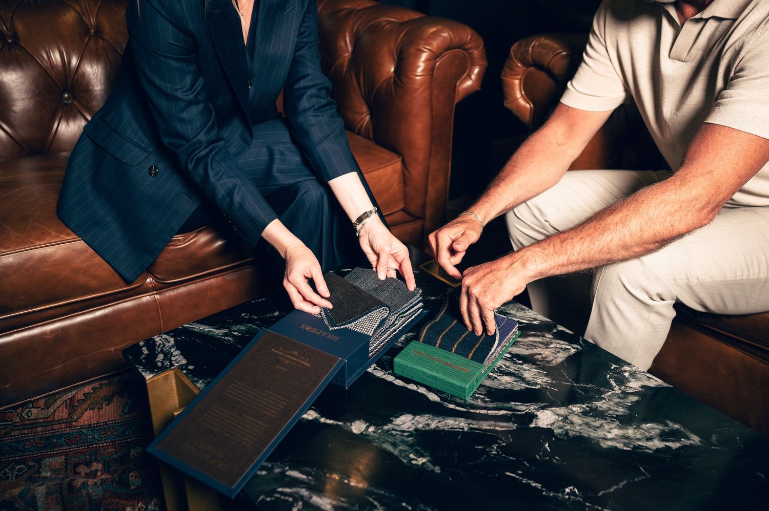 Two professionals examining fabric swatches and leather samples on a marble table in a luxury setting.