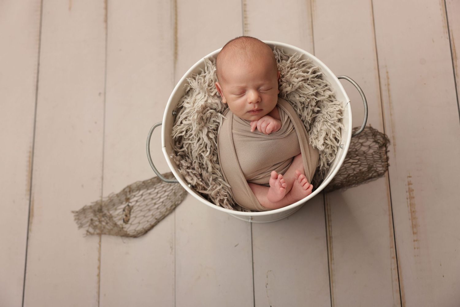 Peaceful newborn baby swaddled in cream wrap sleeping on soft beige blanket during professional newborn photography session.