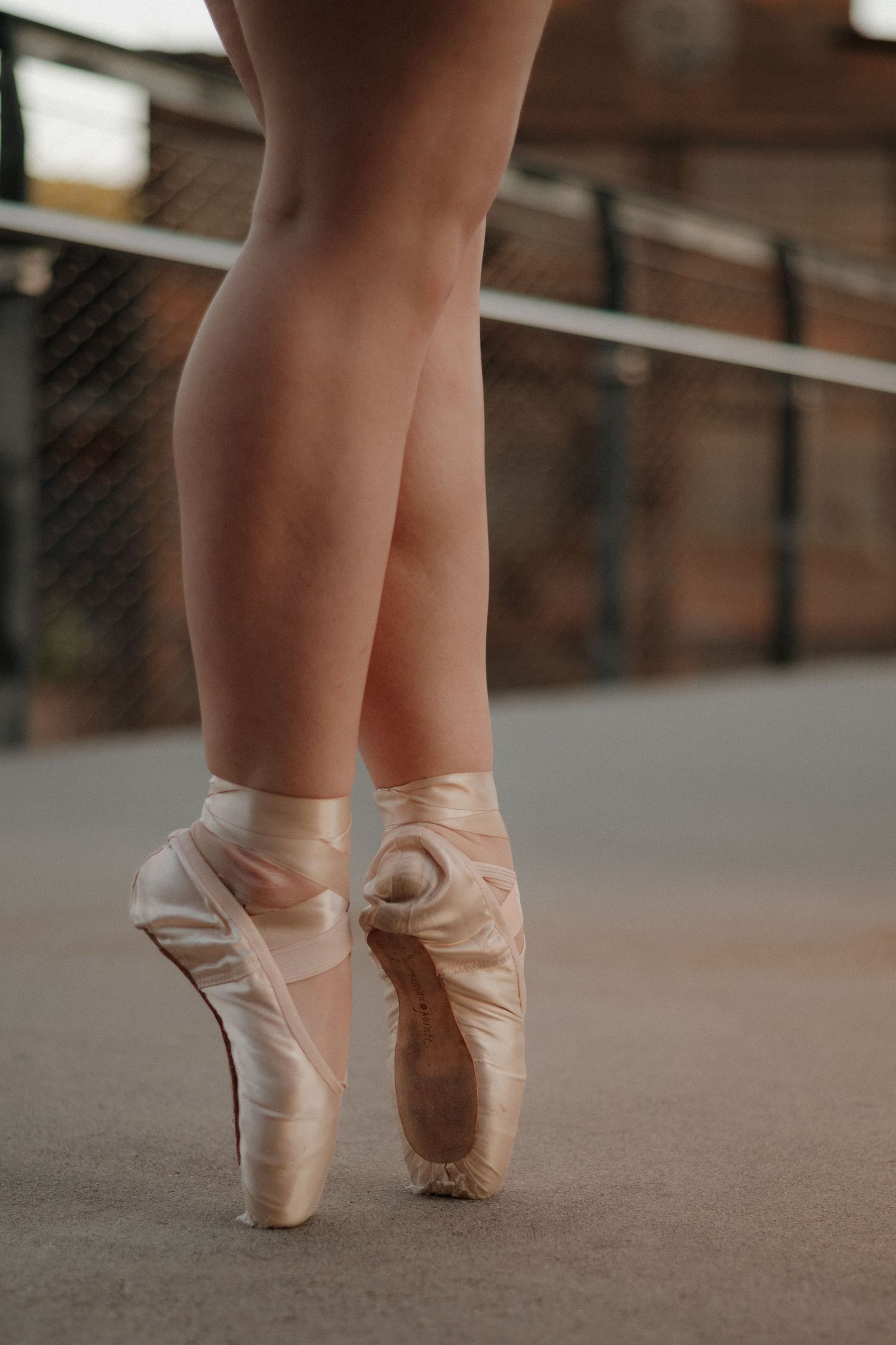 Close-up of a ballerina en pointe in satin ballet shoes on an outdoor urban stage.