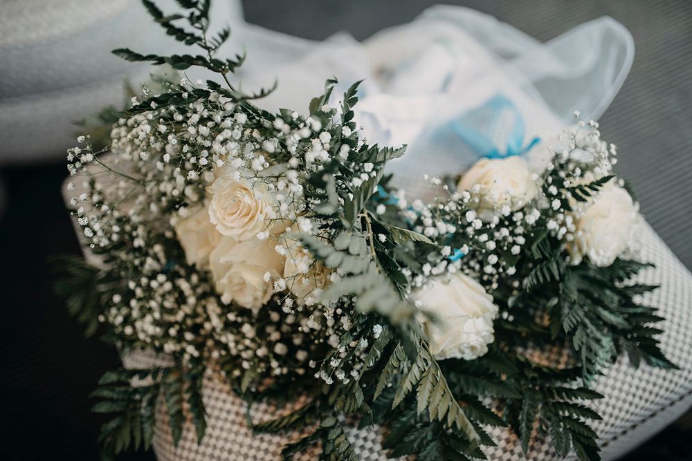 Elegant wedding bouquet of white roses and baby's breath with lush greenery, tied with ribbon.