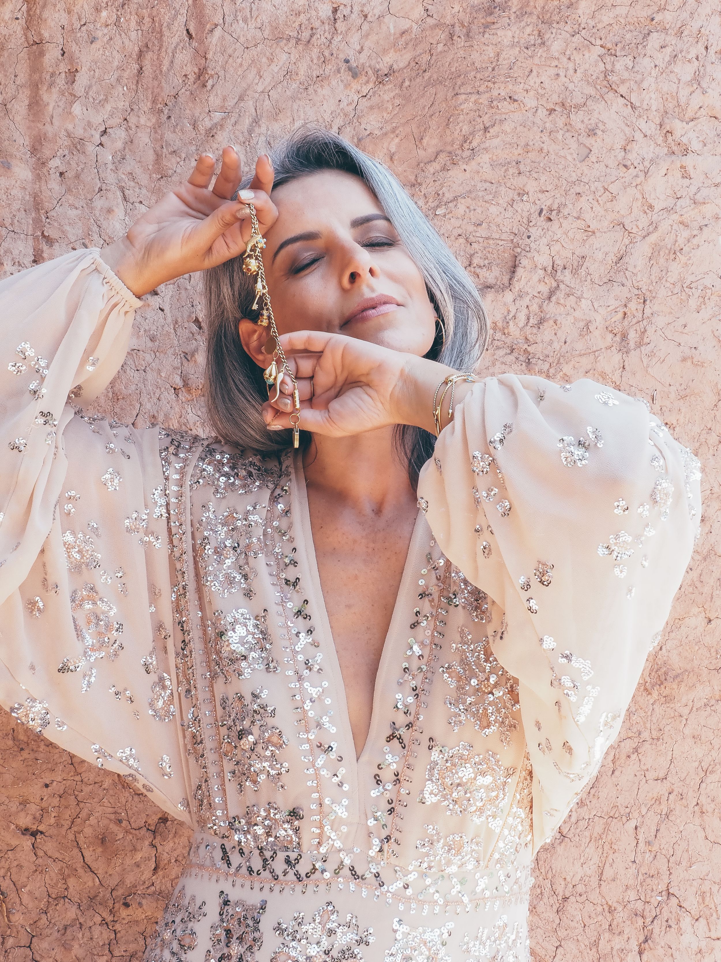 Woman in sequined cream dress with balloon sleeves poses gracefully against a textured beige wall.