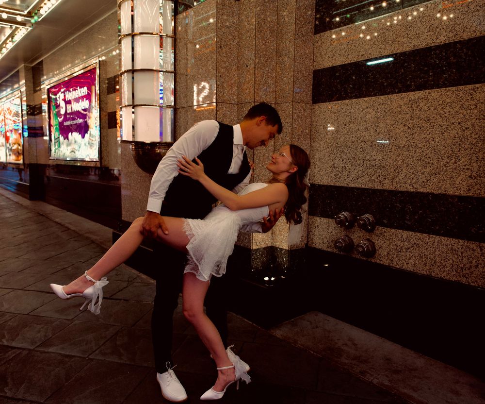 Groom dips bride dramatically outside a glittering Las Vegas building at night.
