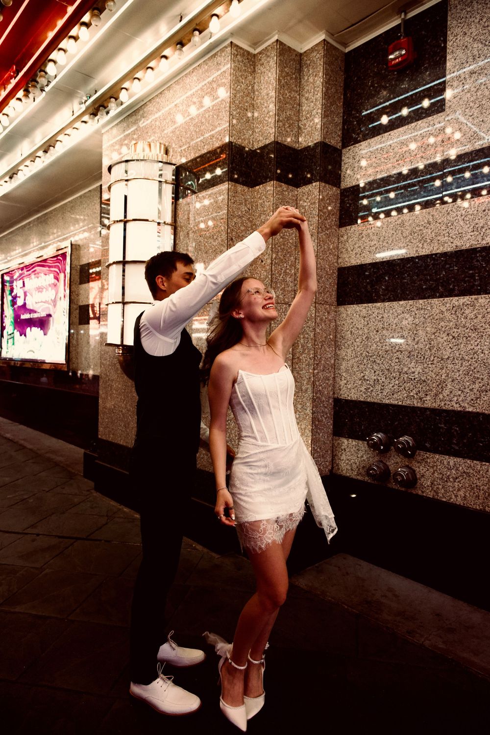 Groom spinning bride in a white mini dress outside a sparkling Las Vegas building.