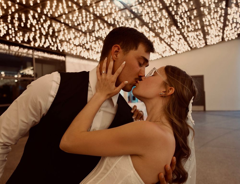 Bride and groom sharing a romantic first dance kiss under sparkling fairy lights at their wedding reception.