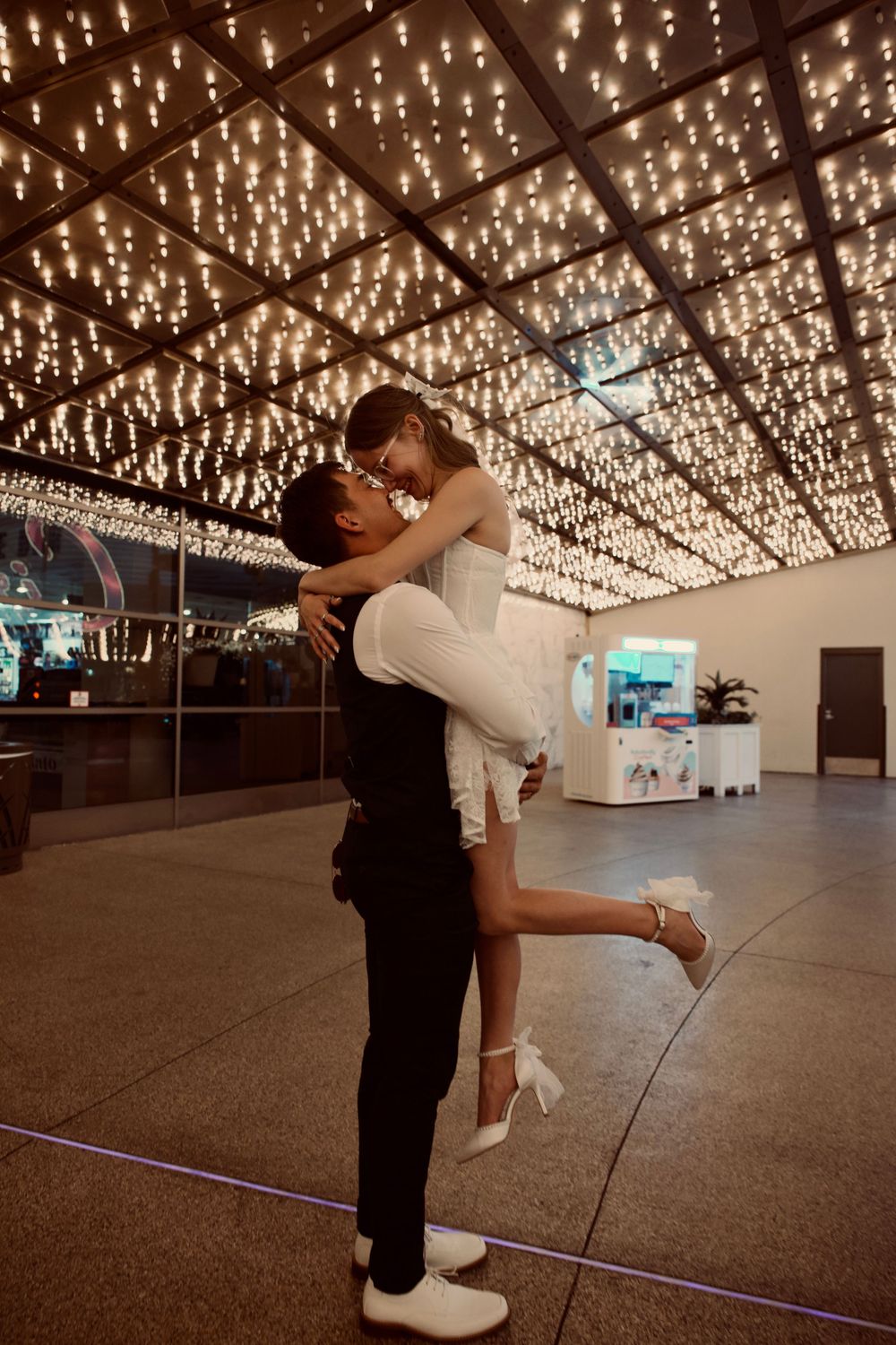 Groom lifting bride under a ceiling of twinkling lights in Las Vegas.
