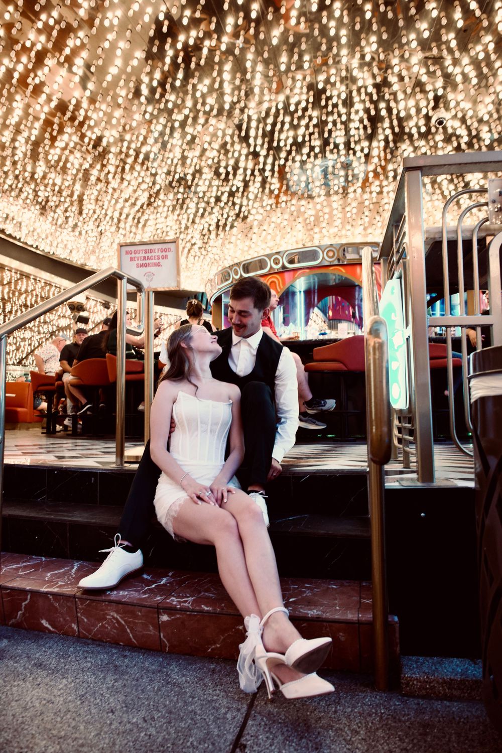 Elegant wedding couple sitting closely together beneath sparkling chandelier lights inside a Las Vegas casino.