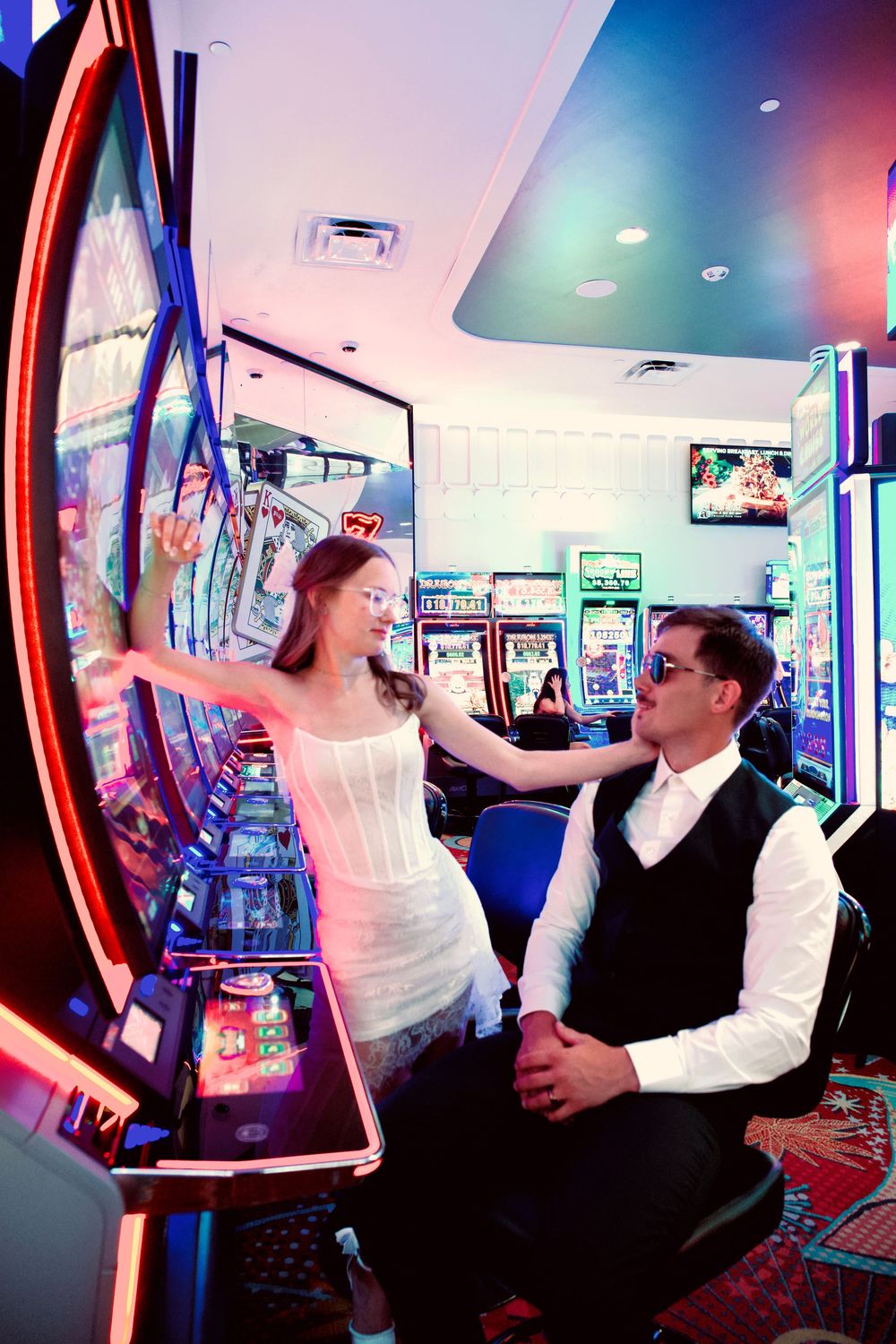 Bride pulling slot machine lever while groom watches with a smile in a colorful Las Vegas casino.