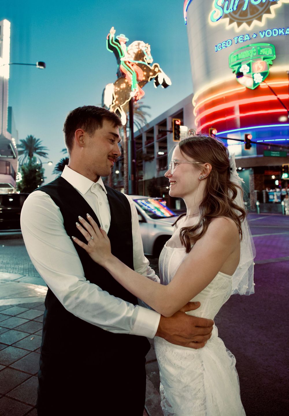 Newlywed couple embracing and smiling on a vibrant Las Vegas street at night with neon signs glowing behind them.